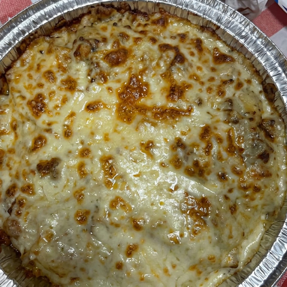 Baked casserole topped with browned melted cheese in a disposable foil dish on a red-and-white checkered tablecloth.